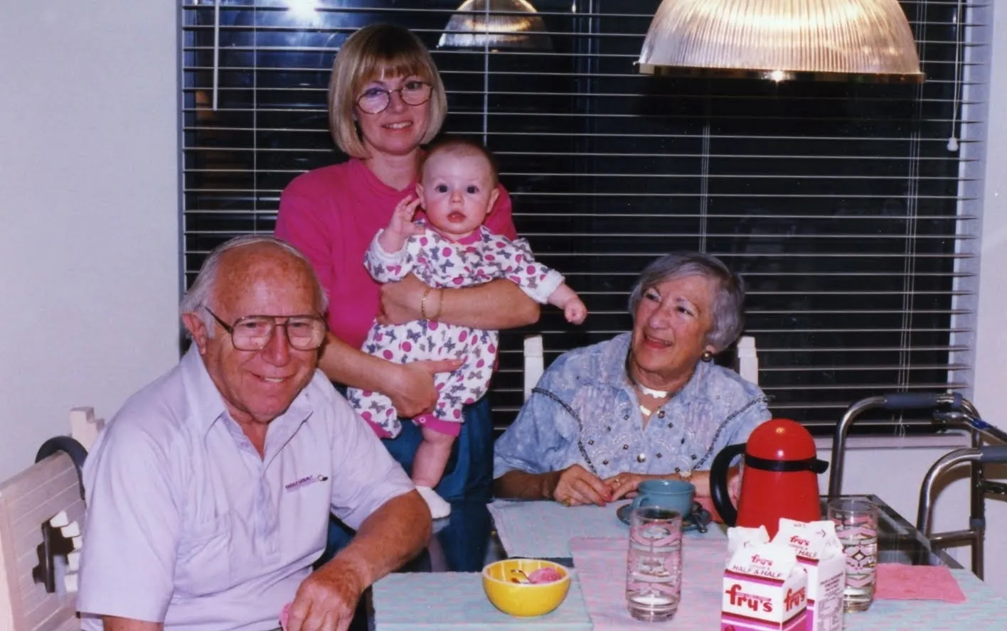 Suzanne holding her baby daughter, standing beside her parents at a table